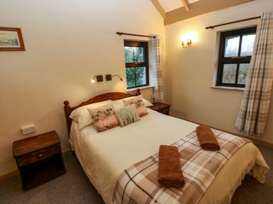 A bedroom with a double bed two bedside tables plaid curtains and two windows at Foxglove in Newport Pembrokeshire