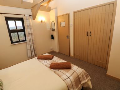 A bedroom with a bed with two towels on the plaid blanket a window with plaid curtains a wooden wardrobe and a door at Foxglove Newport Pembrokeshire