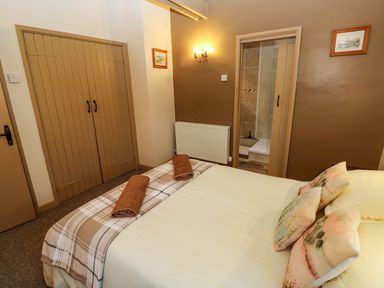 A bedroom with a bed, two rolled towels, a radiator, and a door leading to a bathroom at Foxglove in Newport Pembrokeshire