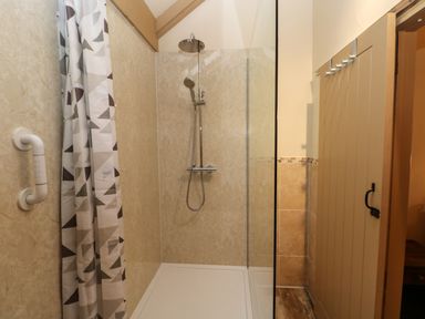A shower area with a curtain a grab handle and a glass panel at Foxglove in Newport Pembrokeshire