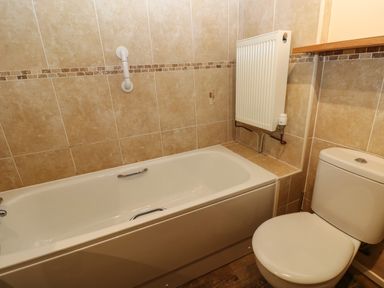 A bathroom with a bathtub a toilet a radiator and tiled walls at Foxglove in Newport Pembrokeshire