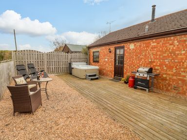 An outdoor patio area with chairs a table a hot tub and a barbecue grill at Dairy Barn in Pershore