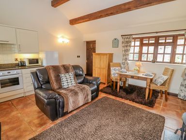 A living area with a black leather sofa a small dining table with two chairs and a kitchen corner at Dairy Barn in Pershore