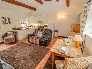 A kitchen and living area with leather sofa wooden dining table and wicker chairs at Dairy Barn in Pershore