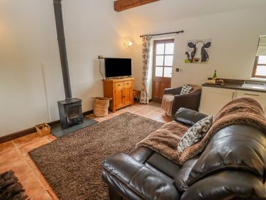 A living room with a wood burner TV on a cabinet and leather sofas at Dairy Barn in Pershore