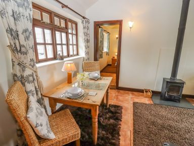 A small dining area with a wooden table set for two next to a window a wood stove and doorway to another room at Dairy Barn in Pershore