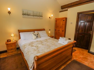A bedroom with a wooden bed frame white bedding and bedside tables with lamps at Dairy Barn Pershore