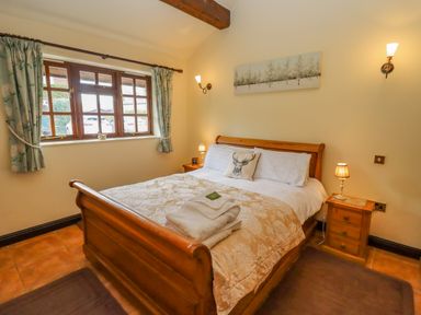 A bedroom with a wooden bed frame white bedding bedside tables and a window with curtains at Dairy Barn in Pershore