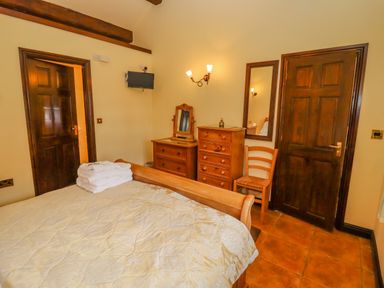 A bedroom with a wooden bed and dressers a chair a wall mirror and a wall-mounted TV at Dairy Barn in Pershore