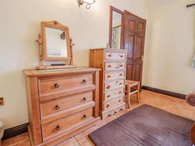 A room with wooden dressers a chair a mirror a brown door and a brown rug on tiled floor at Dairy Barn in Pershore