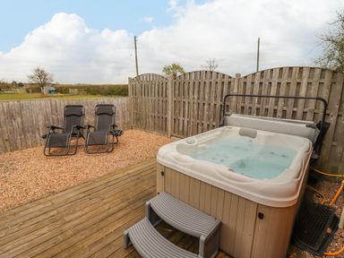An outdoor area with a hot tub and two reclining chairs on gravel with wooden fencing at Dairy Barn in Pershore