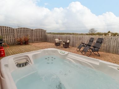 An outdoor area with a hot tub two black recliners a small table with two chairs and a wooden fence at Dairy Barn in Pershore