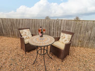 An outdoor seating area with two wicker chairs and a round mosaic table on gravel at Dairy Barn in Pershore