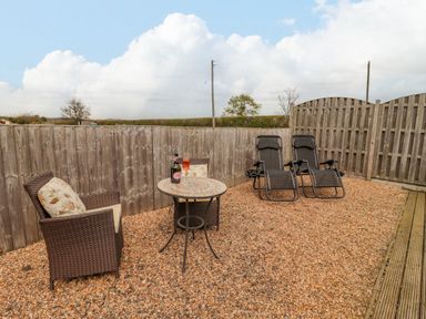 An outdoor seating area with two reclining chairs a table and an armchair on gravel at Dairy Barn in Pershore