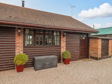 Exterior of a building with a tiled roof two potted plants a window a door and a storage box on a gravel ground at Dairy Barn in Pershore