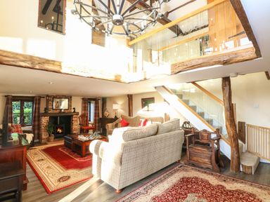 A living room with sofas a fireplace and a staircase with glass railing at The Barn Saham Hills near Swaffham