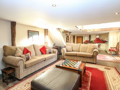 A living room with two sofas a chess board a leather ottoman and a kitchen area at The Barn in Saham Hills near Swaffham