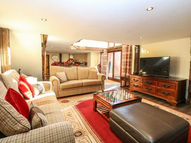 A living room with sofas cushions a chessboard on a coffee table a large ottoman and a television on a wooden cabinet at The Barn Saham Hills near Swaffham