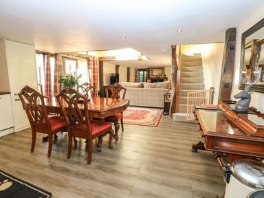 A dining area with wooden table and chairs next to a living room with a sofa and carpet at The Barn in Saham Hills near Swaffham