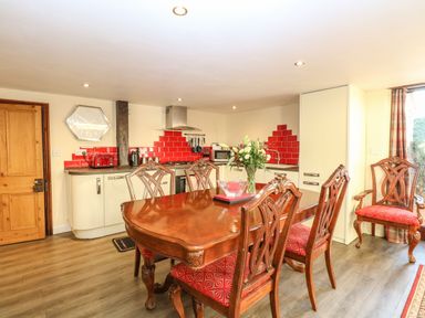 A kitchen and dining area with a wooden dining table and chairs with red cushions and red tiled backsplash at The Barn Saham Hills near Swaffham