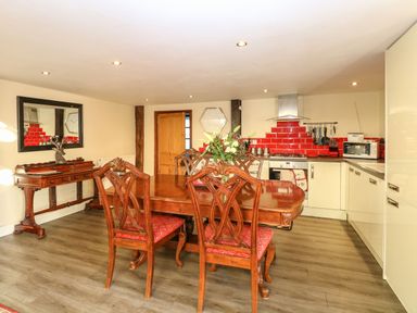 A kitchen with wooden dining table and chairs red tiled backsplash and white cabinets at The Barn in Saham Hills near Swaffham