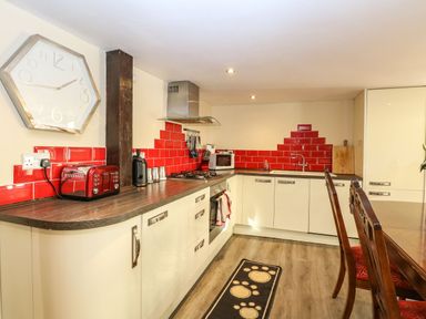 A kitchen with red tiles on the wall white cabinets a wooden countertop and dining chairs at The Barn Saham Hills near Swaffham