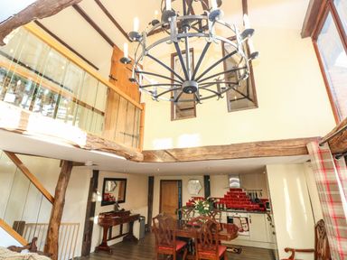 A dining area with wooden table and chairs under a large chandelier at The Barn Saham Hills near Swaffham