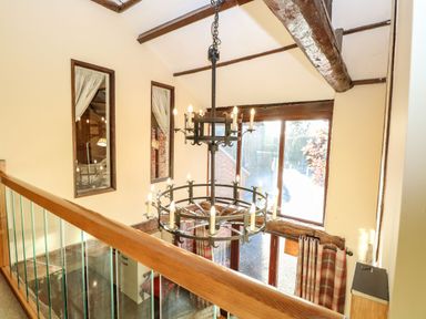Interior view of a two-story space with wooden beams a chandelier and large windows with curtains at The Barn Saham Hills near Swaffham