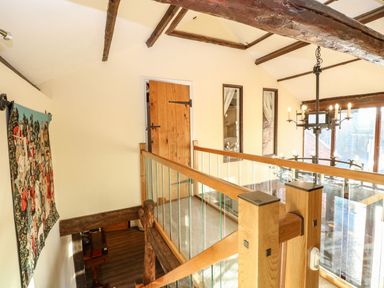 An upstairs hallway with wooden beams glass railings a wooden door and a tapestry on the wall at The Barn Saham Hills near Swaffham