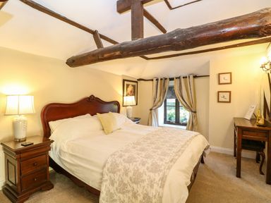 A bedroom with a bed lamp two nightstands window with curtains and wooden beams at The Barn Saham Hills near Swaffham