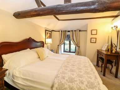 A bedroom with a large wooden bed white bedding a window with curtains and a wooden dressing table at The Barn Saham Hills near Swaffham