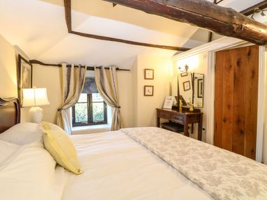 A bedroom with a bed curtains a window a lamp a dressing table with mirrors and framed pictures on the wall at The Barn Saham Hills near Swaffham