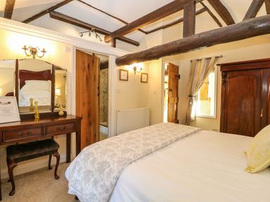A bedroom with a bed a wooden dresser with a mirror a stool wooden beams and a wardrobe at The Barn in Saham Hills near Swaffham