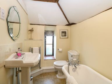 A bathroom with a pedestal sink mirror toilet clawfoot bathtub and small window at The Barn Saham Hills near Swaffham