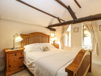 A bedroom with a wooden bed frame two bedside tables and exposed wooden beams at The Barn Saham Hills near Swaffham