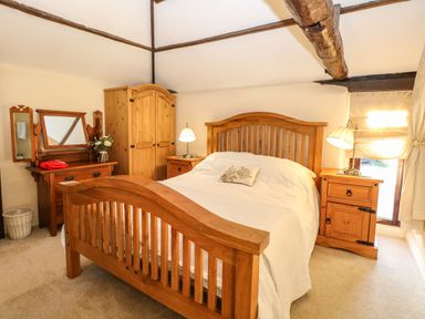 A bedroom with a wooden bed frame bedside tables wardrobe and vanity at The Barn Saham Hills near Swaffham