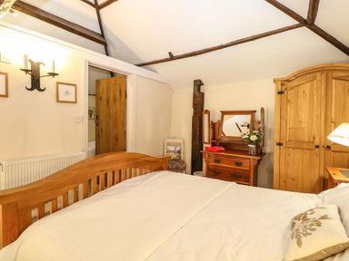 A bedroom with a wooden bed wardrobe and dresser with mirror at The Barn Saham Hills near Swaffham