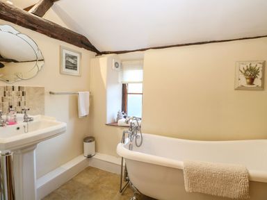 A bathroom with a freestanding bathtub a pedestal sink a towel on a rack and a window at The Barn in Saham Hills near Swaffham