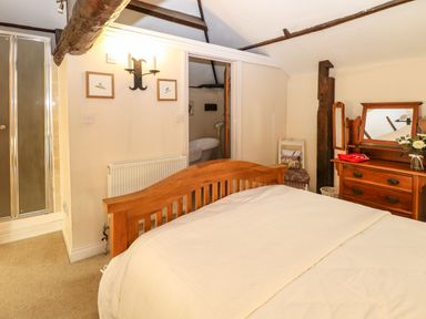 A bedroom with a wooden bed frame a dresser with a mirror a chair and an open door showing a bathroom at The Barn Saham Hills near Swaffham