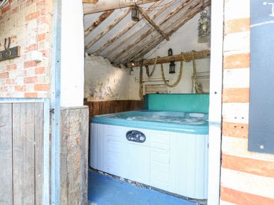 A room with a hot tub under a wooden beam ceiling with hanging lanterns at The Barn Saham Hills near Swaffham
