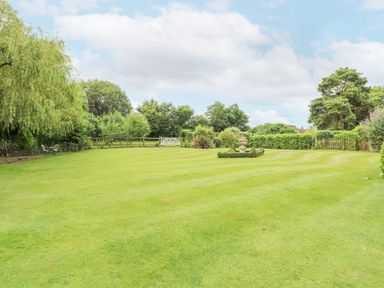 A large grassy garden with trimmed hedges and trees surrounding it at The Barn in Saham Hills near Swaffham