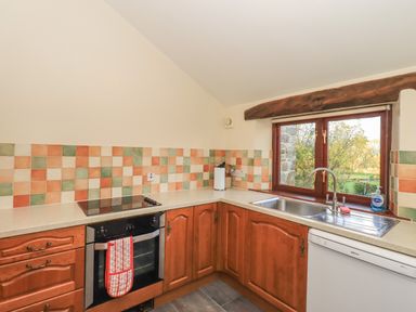 A kitchen with brown cabinets a built-in oven a cooktop a sink under a window and multicolored tiled backsplash at Hadrian's View in Banks near Brampton