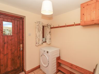 A utility room with a washer dryer wooden door window with floral curtains and wooden bench at Hadrians View Banks near Brampton