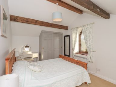 A bedroom with wooden bed frame a grey wardrobe a dressing table and a window with floral curtains at Hadrians View Banks near Brampton