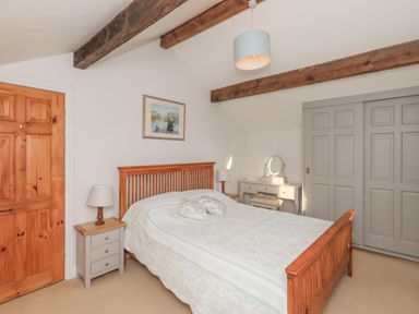 A bedroom with a wooden bed frame two bedside tables lamps a dressing table and gray sliding wardrobes at Hadrian's View Banks near Brampton