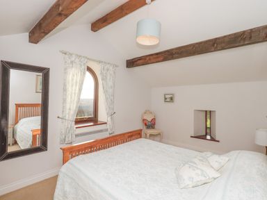 A bedroom with a wooden bed frame a large mirror curtains on an arched window and exposed wooden ceiling beams at Hadrians View Banks near Brampton