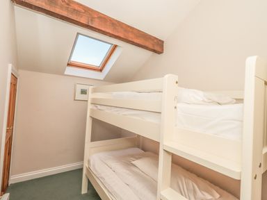 A bedroom with white bunk beds a skylight window wooden beam and a wooden door at Hadrians View Banks near Brampton