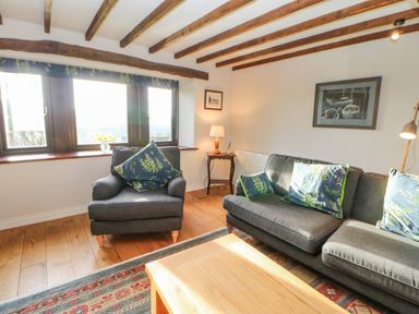 A living room with a dark armchair and sofa with patterned cushions wooden coffee table and exposed wooden ceiling beams at Hadrians View Banks near Brampton