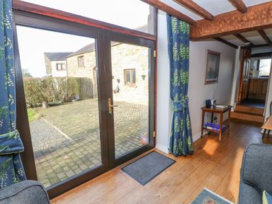 A room with wooden floors beams blue curtains and glass doors opening to a paved courtyard at Hadrians View Banks near Brampton