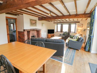 A living room with a dining table exposed wooden beams and a fireplace at Hadrians View Banks near Brampton